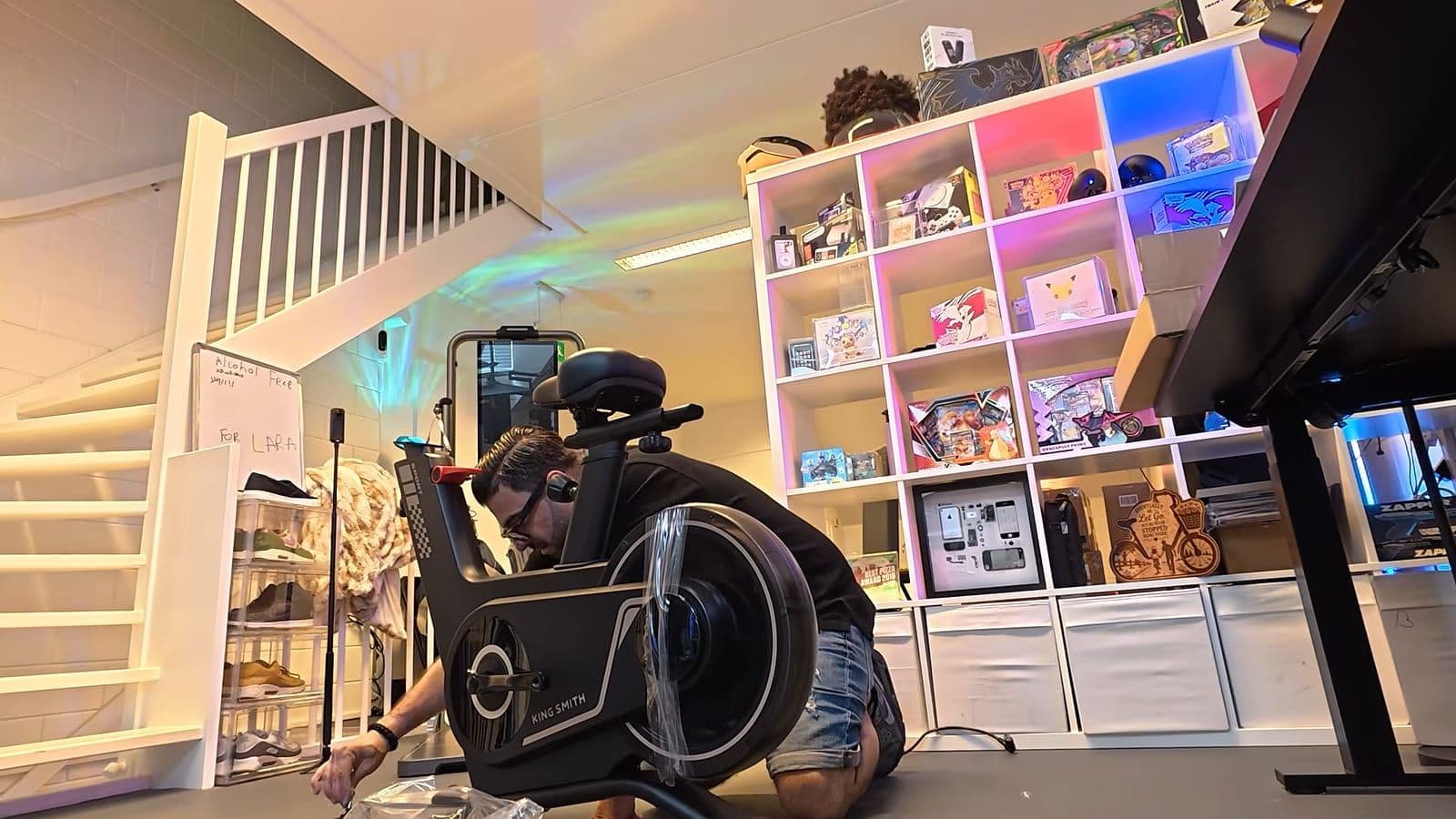 Zino zet de zwarte KingSmith spinningfiets in elkaar op de vloer van zijn studio, met plastic nog om het vliegwiel