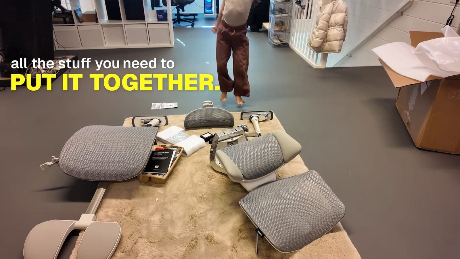 Parts of the Hbada X7 chair laid out on the carpet including the seat base, backrest, and assembly hardware