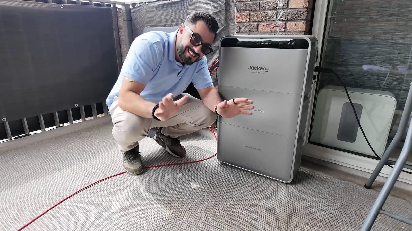 Zino gehurkt op het balkon naast de Jackery SolarVault 3 Pro Max toren met twee extra accumodules