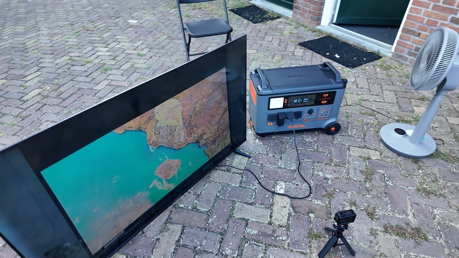 Oscal PowerMax 6000 op een klinkeroprit, aangesloten op een grote tv en een staande ventilator
