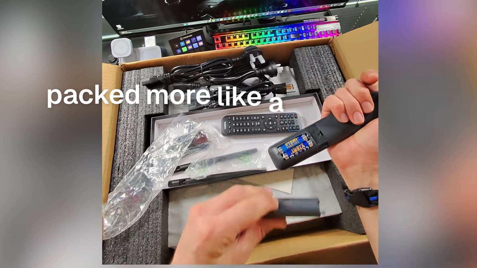 Hand holding one of the two remote controls above the open packaging box