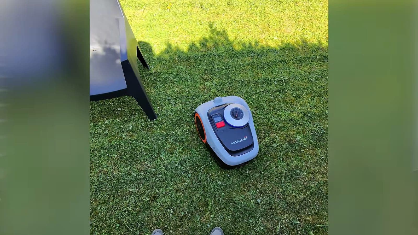 Schuin bovenaanzicht van de compacte robotmaaier die strak langs het tuinmeubilair rijdt