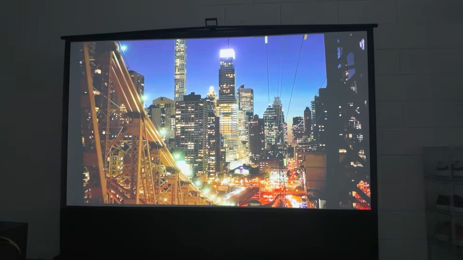 Ultimea Poseidon E100 projecting a vibrant cityscape onto a pull-up projector screen in a dark room