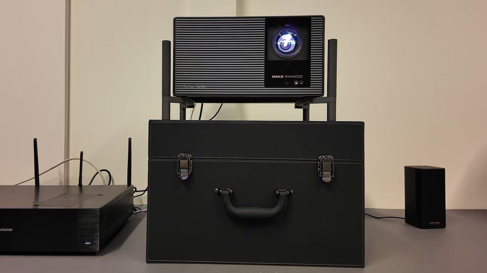 Zino sitting next to the XGIMI TITAN Noir Max sitting atop its leather-style travel suitcase